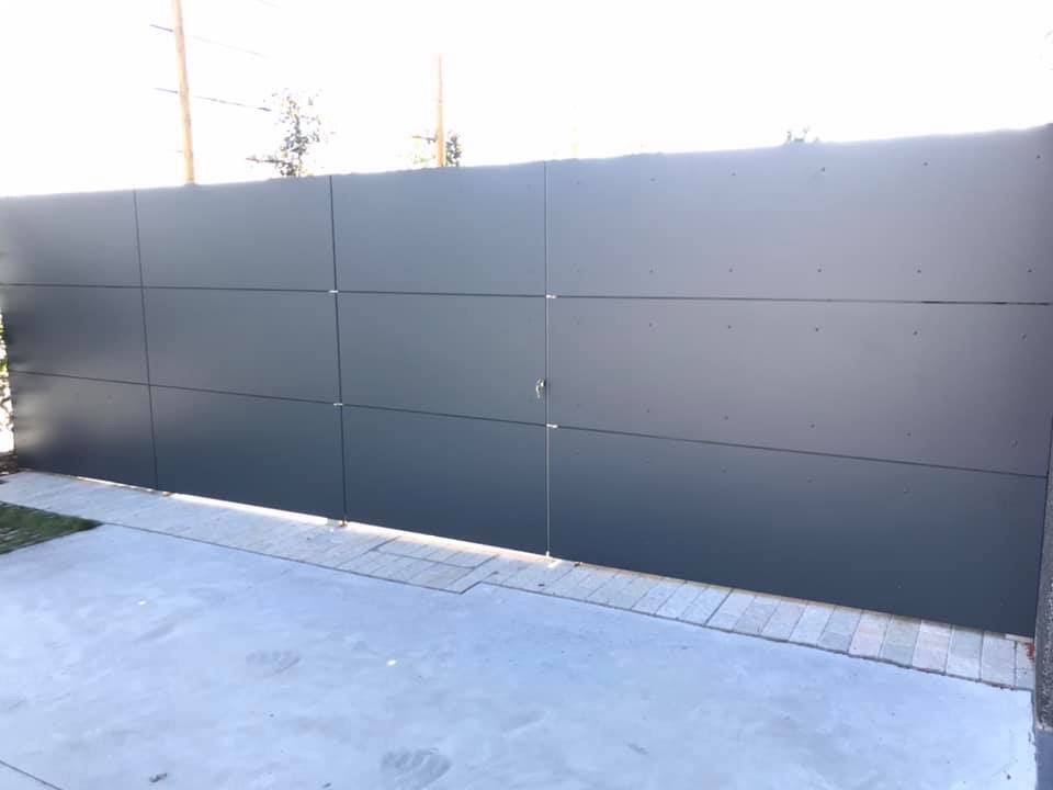 Strakke Trespa wand met onzichtbaar geïntegreerde poort in een moderne tuinomgeving.