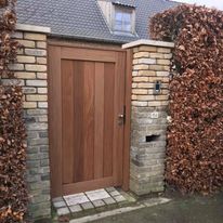 Tuinpoort in afrormosia hout tussen bakstenen zuilen in Handzame