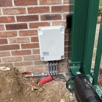 Netjes afgewerkte sturingskast voor poortautomatisatie, gemonteerd tegen een muur.