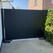 Moderne aluminium dubbele draaipoort in donkere kleur, geplaatst aan een oprit.