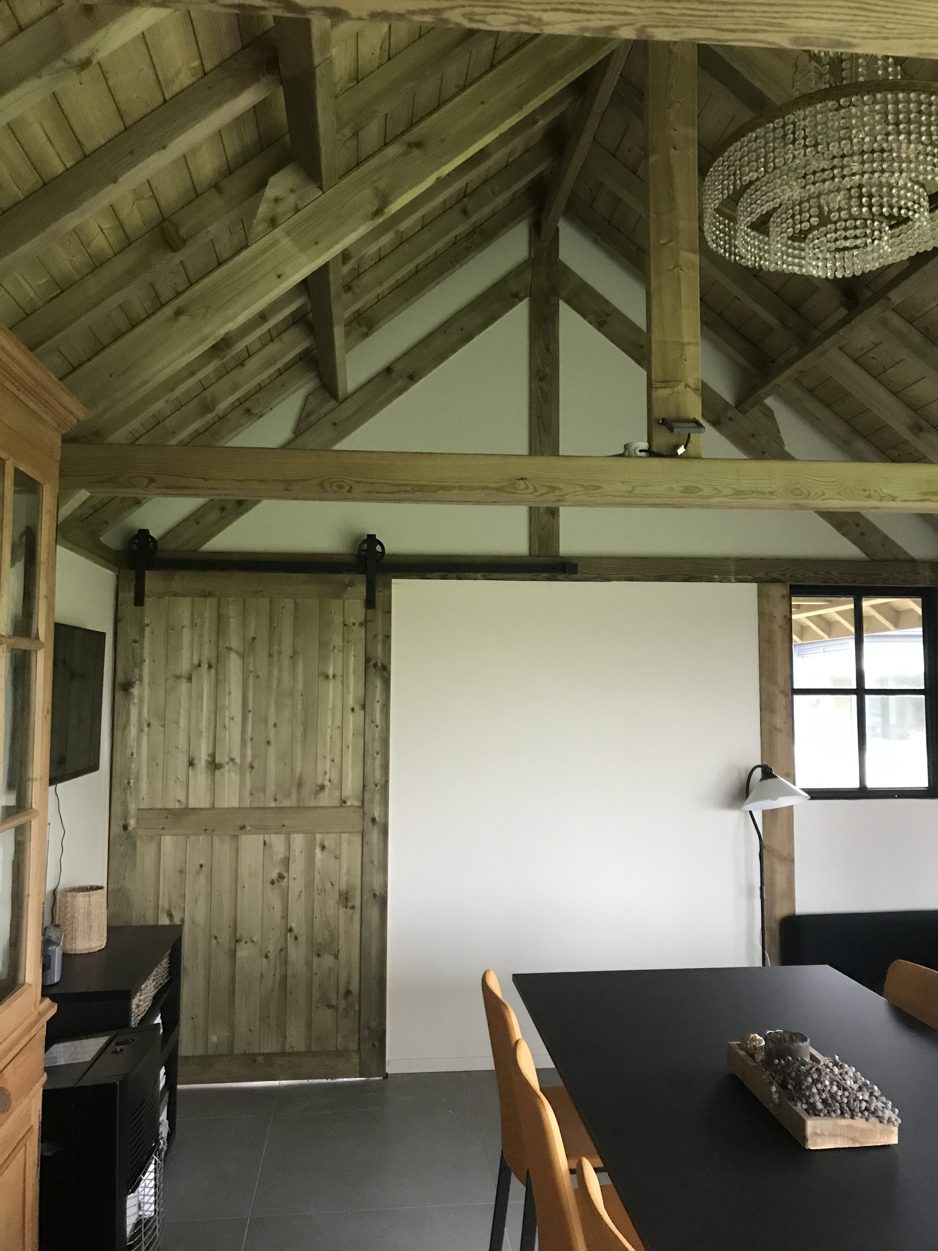 Binnenafwerking van een houten bijgebouw met zichtbare balken en schuifdeur