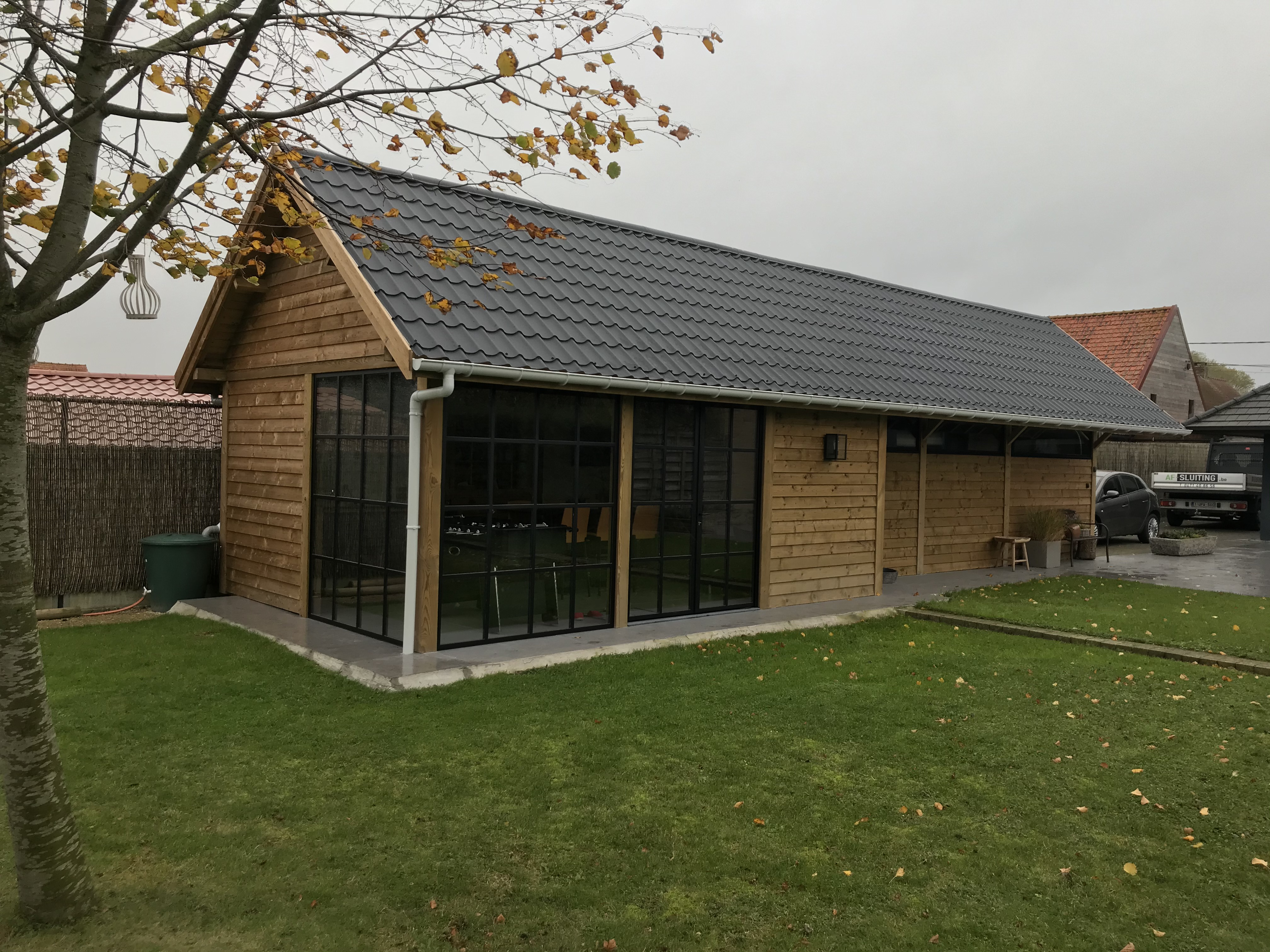Houten bijgebouw met grote ramen en pannendak in een tuin