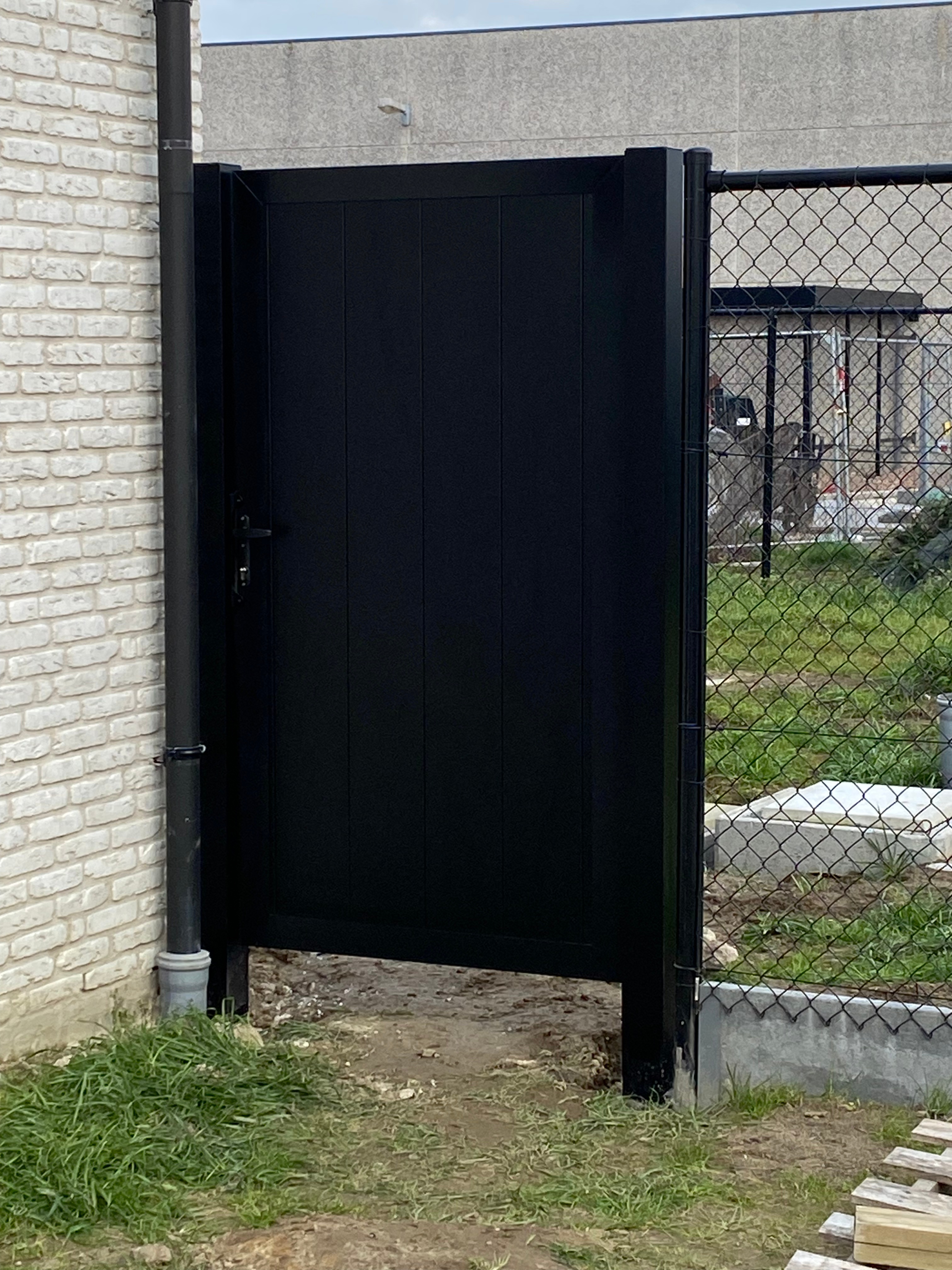 Zwarte aluminium tuinpoort geplaatst naast een woning in Handzame.