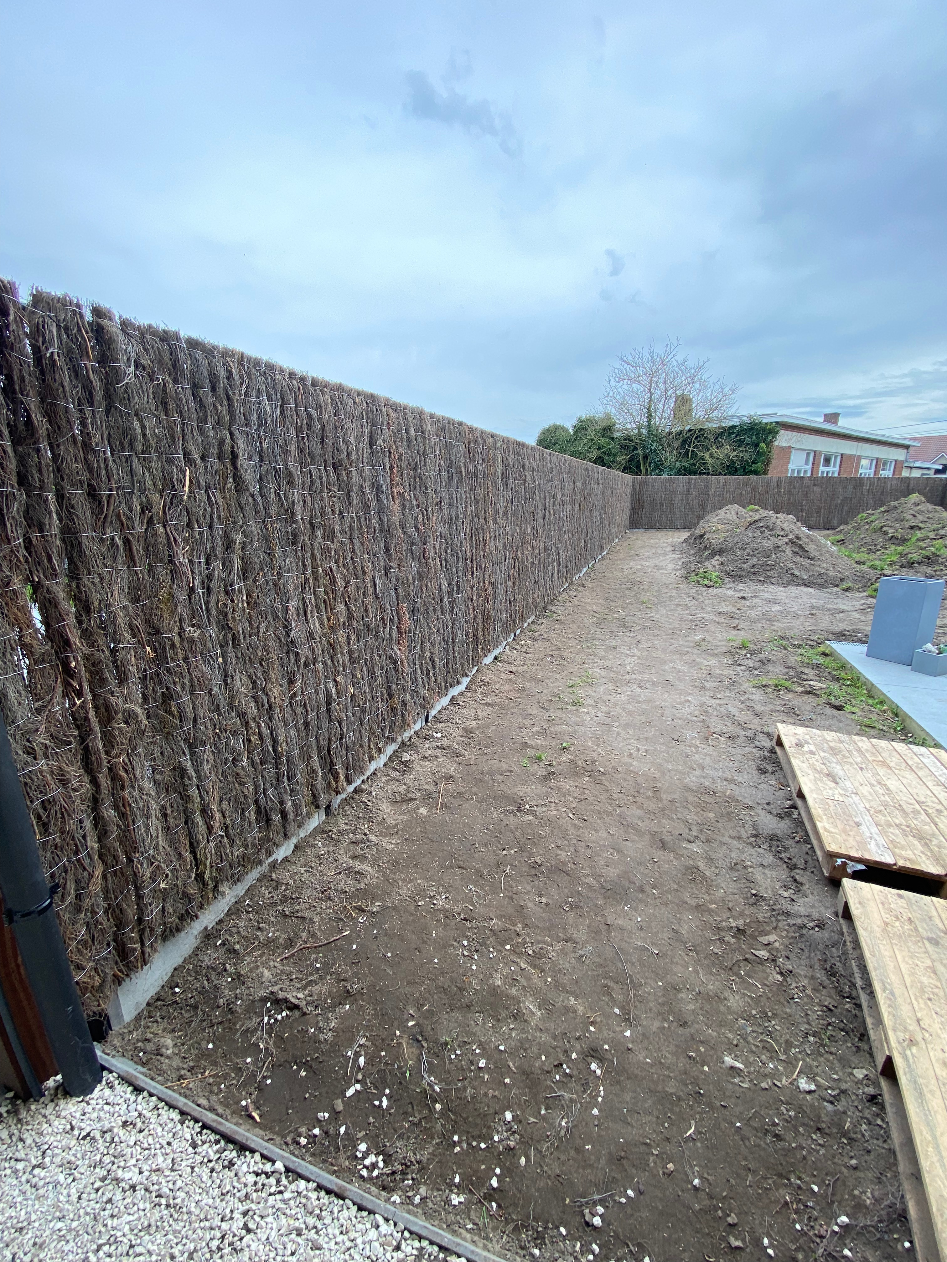 Draadafsluiting met ericamatten voor privacy en betonplaat onderaan, geplaatst in Kortemark.