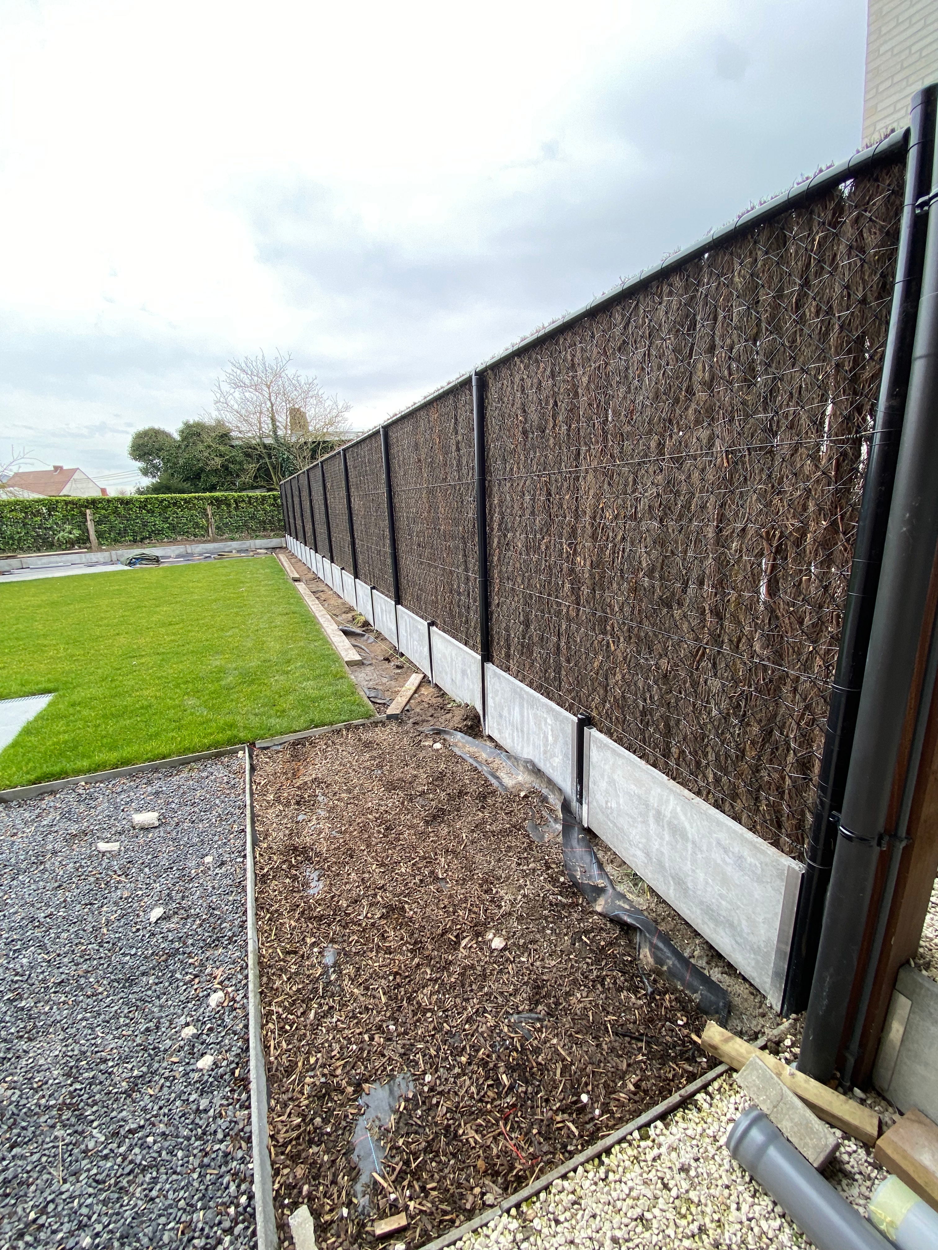 Draadafsluiting met ericamatten voor privacy en betonplaat onderaan, geplaatst in Kortemark.