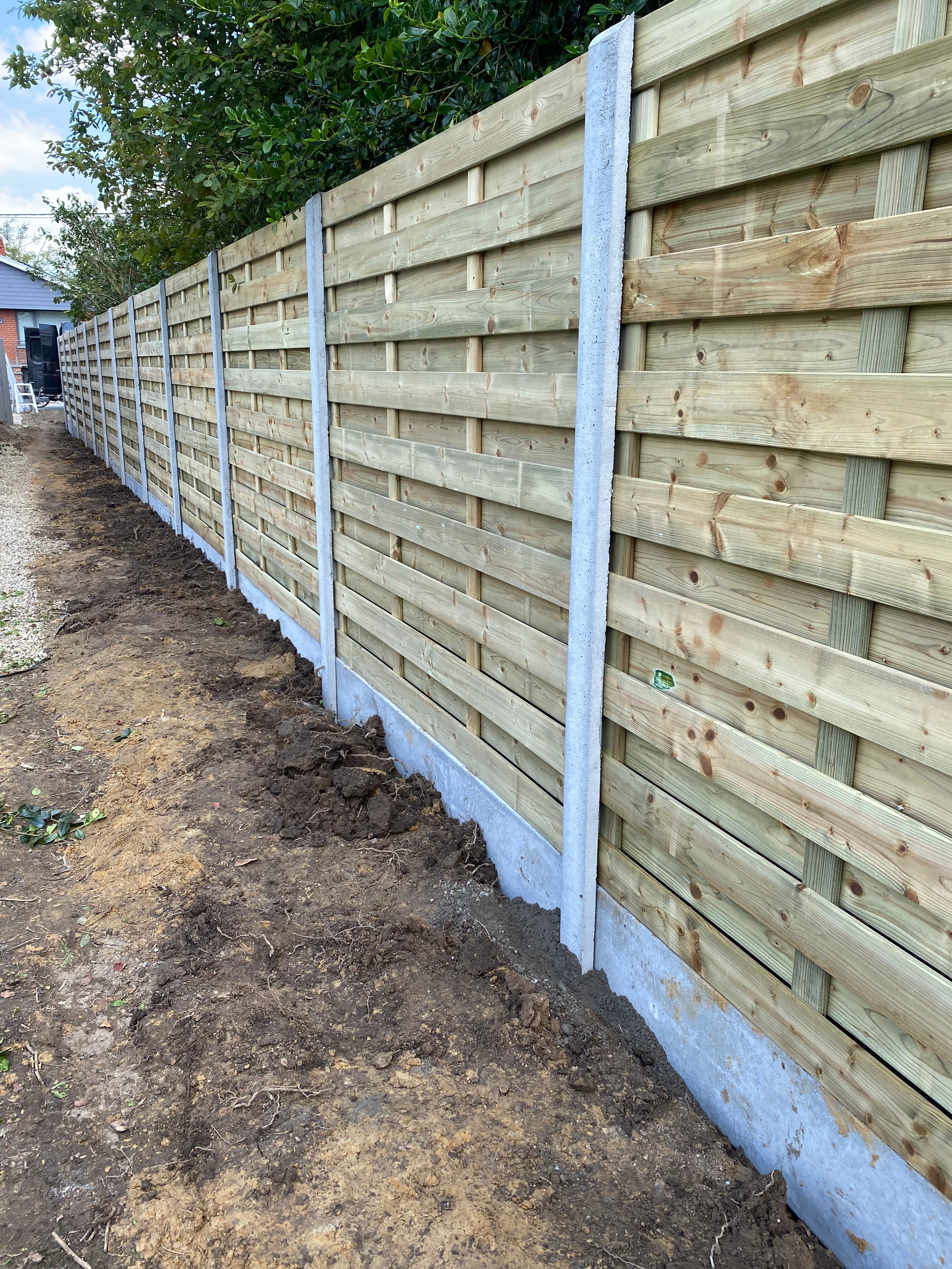 Houten afsluitingspanelen geplaatst tussen betonpalen met betonplaat onderaan, in Staden.