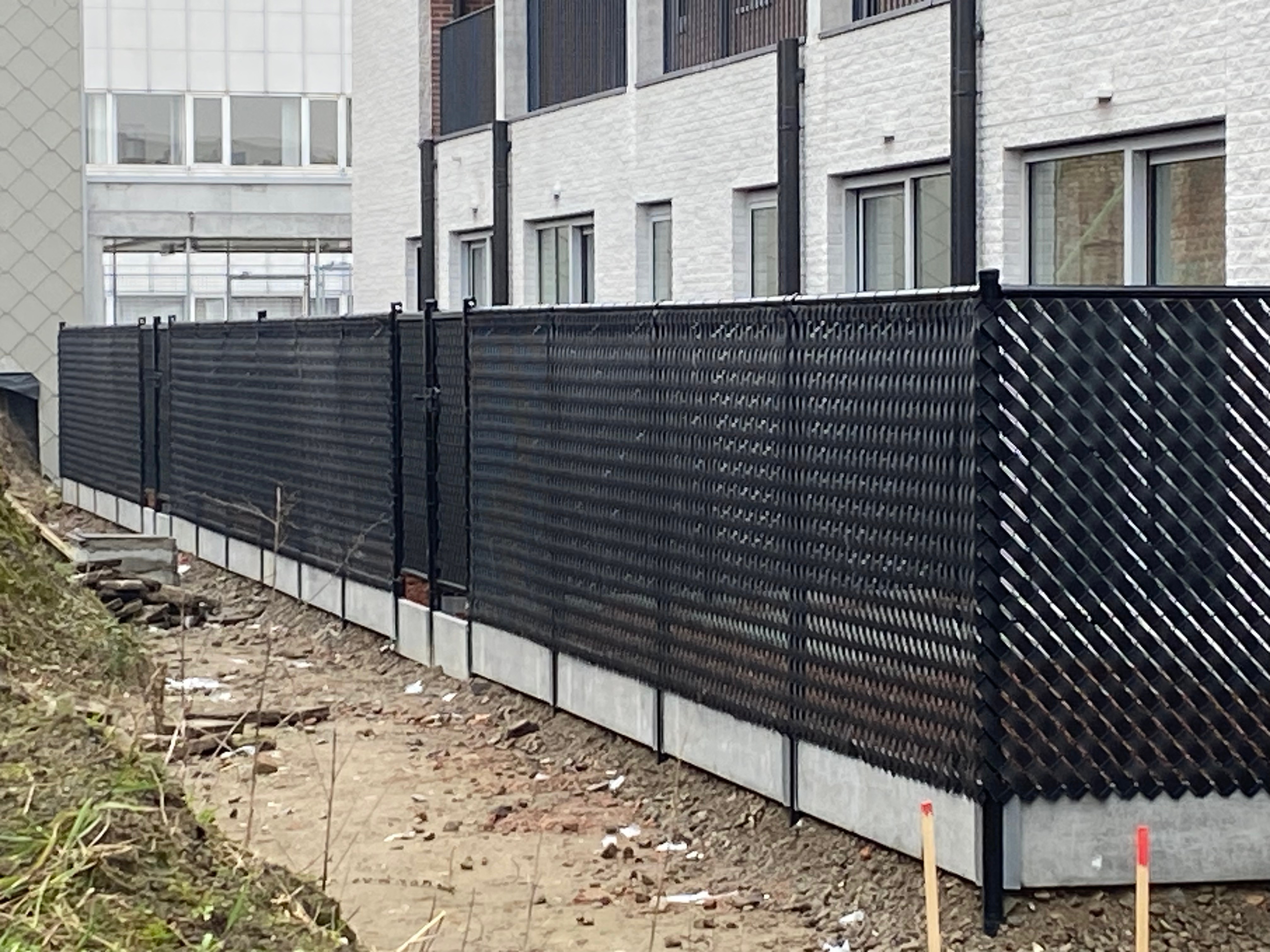 Draadafsluiting met zwarte PVC-lamellen voor privacy, geplaatst op betonplaten in Sint-Niklaas.